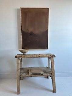 a wooden table with a bowl on it in front of a wall mounted art piece