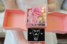 a person holding a pink box with jewelry in it's hands and flowers on the inside