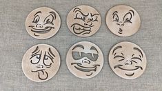 four wooden coasters with faces drawn on them, all in different shapes and sizes