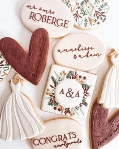 decorated cookies with names and wedding gowns are arranged on a white tablecloth in the shape of hearts