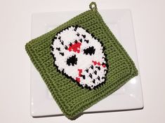 a white plate topped with a green crocheted dishcloth and a skull on it