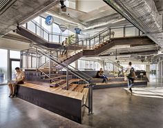 people are sitting on the stairs in an office building with glass walls and steel railings