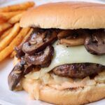 a cheeseburger with mushrooms is on a plate next to french fries