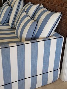 a blue and white striped couch sitting in front of a brick wall with pillows on it