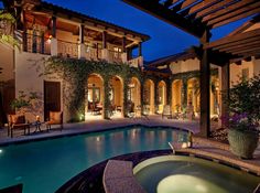 an outdoor swimming pool surrounded by patio furniture and plants at night time with lights on