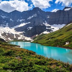 the mountains are covered with snow and blue water in the foreground is a lake surrounded by lush green vegetation