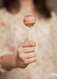 a woman holding a pink frosted donut on a stick