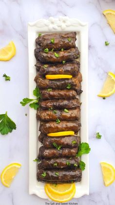 grilled meat with lemons and parsley on a white platter surrounded by sliced lemon wedges