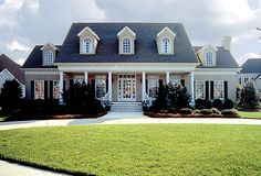 a large white house with black shutters on the front and side windows, surrounded by lush green grass