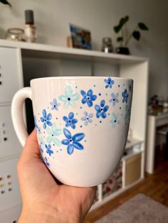 a hand holding a coffee cup with blue flowers painted on the outside and inside, in front of a white cabinet