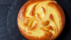 a pastry with yellow icing on it sitting on a black surface next to a spoon