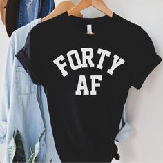 a black shirt with the words fifty af on it hanging next to some jeans and a denim jacket