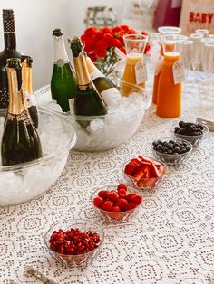 bottles of champagne and berries on a table with bowls of fruit in the foreground