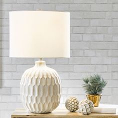 a white table lamp sitting on top of a wooden table next to a potted plant