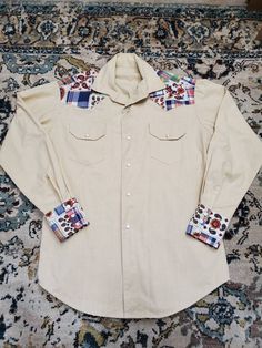 "Amazing one of a kind vintage handmade western top! Probably from the 70's! Thick textured cream fabric with printed patchwork accents (floral, paisley, plaid) on sleeve cuffs and around collar. Cute horseshoe snaps! Down front and 3 on each sleeve cuff. Pockets in front. In Excellent Vintage Condition with no visible flaws! Measurements: Chest: 44\" Length: 29\" Shoulders: 18.5\" Sleeve Length: 33.5\"" Western Style Cotton Shirt For Spring, Vintage Cotton Tops For Rodeo, Fitted Cotton Western Top, Fitted Collared Patchwork Top, Fitted Patchwork Collared Top, Fitted Plaid Western Tops, Fitted Western Plaid Tops, Fitted Long Sleeve Tops With Floral Patchwork, Fitted Cream Tops With Button Cuffs