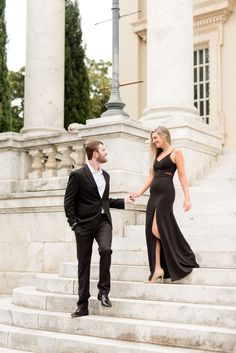 a man and woman in formal wear standing on the steps of a building holding hands