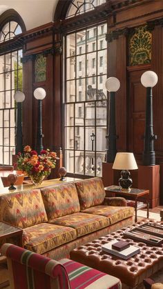 a living room filled with lots of furniture next to tall windows and lamps on either side of the couch