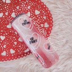 a pink water bottle sitting on top of a red doily with hearts around it