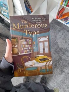 a person holding up a book in front of a table with a typewriter on it