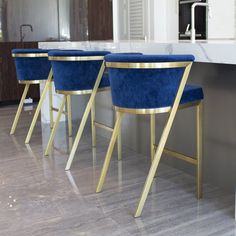 three blue velvet bar stools sitting in front of a kitchen island with marble counter tops