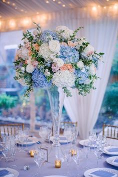 a tall vase filled with blue and white flowers on top of a dining room table