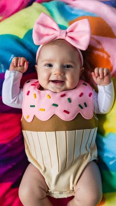 a smiling baby wearing a pink and brown cupcake costume on top of a colorful blanket