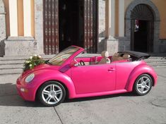 a pink convertible car parked in front of a building with flowers on the hood and windows