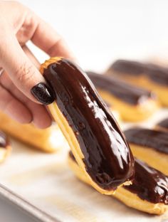 a person holding a chocolate covered donut on a tray with other donuts in the background