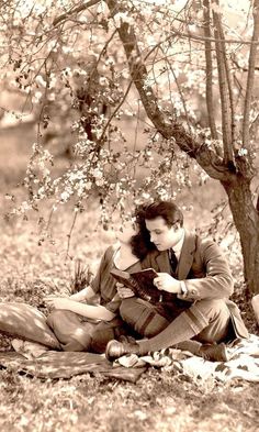 a man and woman sitting on the ground under a tree with their arms around each other