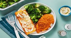 a white plate topped with fish and broccoli next to a bowl of dip