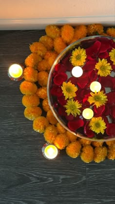 a bowl with candles and flowers in it on the floor next to some orange balls