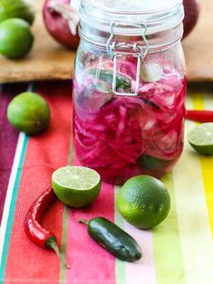 a jar filled with pickles and onions on top of a striped table cloth next to limes