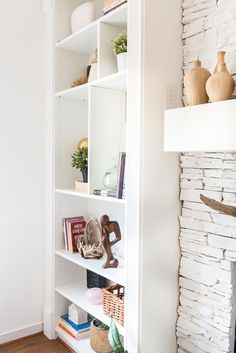 a white book shelf filled with books next to a fire place and vases on top of it