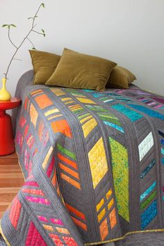 a bed with a colorful quilt on top of it next to a vase and lamp