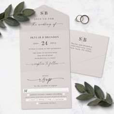 the wedding stationery is laid out on a marble table with greenery and rings