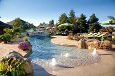 an outdoor swimming pool surrounded by rocks and water features waterfall, umbrellas and lawn chairs