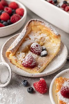 a piece of cake on a plate with berries and powdered sugar