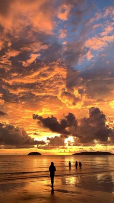 people walking on the beach at sunset with clouds in the sky and one person holding an umbrella