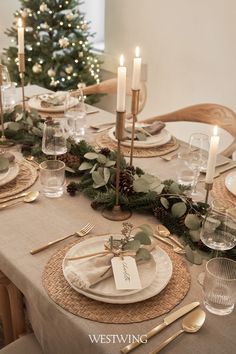 the table is set for christmas dinner with candles and greenery on each place setting