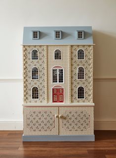 a doll house with three floors and two windows on the top floor, in front of a white wall