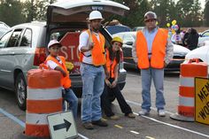 three people in orange vests standing next to traffic cones and signs with cars behind them