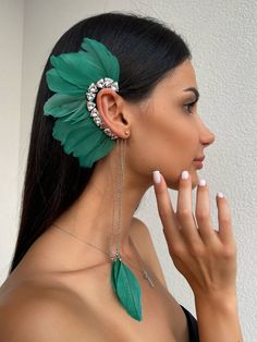 a woman with long black hair and green feathers on her head, wearing ear clips