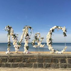 the word love spelled out with flowers on a brick wall near the ocean and blue sky