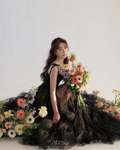 a woman in a black dress sitting on the ground surrounded by flowers