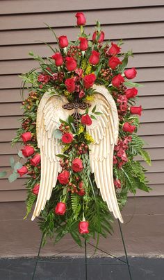 a white angel with red roses and greenery in front of a wall behind it