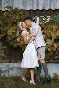 a man and woman standing next to each other in front of a wooden fence with ivy growing on it