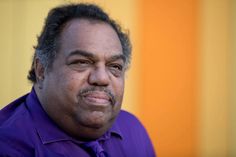 a man in a purple shirt and tie looking at the camera with an intense look on his face