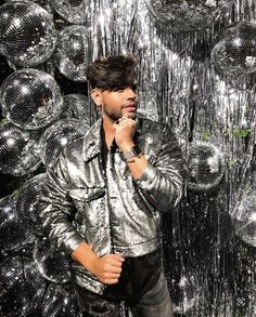 a man standing in front of silver disco balls with his hands to his face and holding a microphone