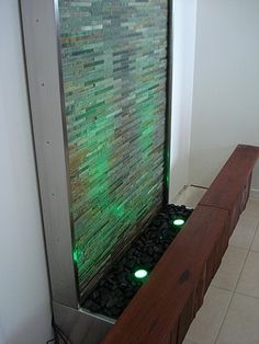 a water fountain with green lights in the middle of a tiled floored area next to a white wall