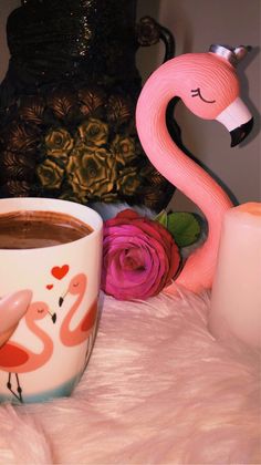 a pink flamingo coffee cup sitting on top of a table next to a candle